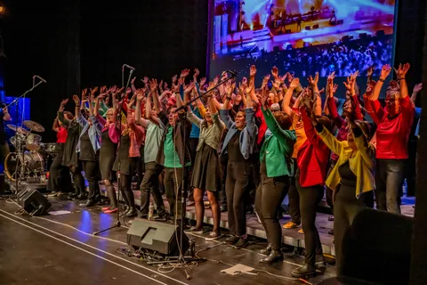 Der komplette Chor colorsounds jubelt mit erhobenen Armen auf der Konzertbühne