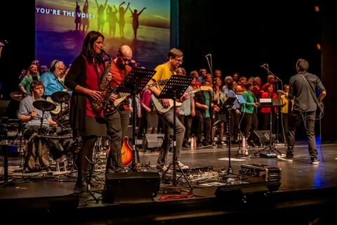 Die Band von colorsounds mit Saxofon und Gitarren vor dem singenden Chor