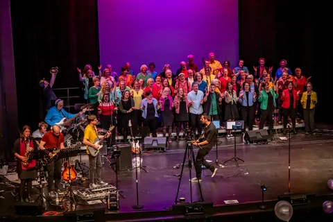 Bühnenansicht mit Band und Chor colorsounds vor violett beleuchtetem Hintergrund